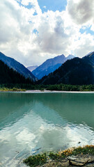 Obraz premium High mountains covered with pine and spruce forests and a deep lake at the foot, on a sunny summer day, against the backdrop of a sky with clouds.