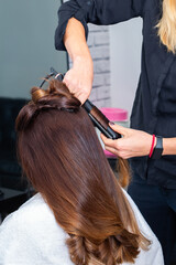 Naklejka premium Hairdresser making hairdo using curling iron to straighten hair