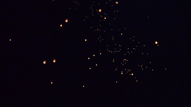 A glowing sky lantern being released into a starry night, surrounded by a mesmerizing cluster of floating lanterns, symbolizing hope, dreams, and celebration under the vast dark sky