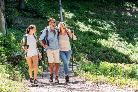 A family enjoys hiking together in nature on a sunny summer day. They walk along a trail, taking in the beautiful surroundings and sharing smiles and laughter.	
