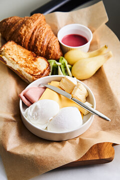 A delightful brunch platter includes various cheeses, fresh fruit, and a croissant, all elegantly arranged on a wooden board, showcasing a vibrant breakfast selection