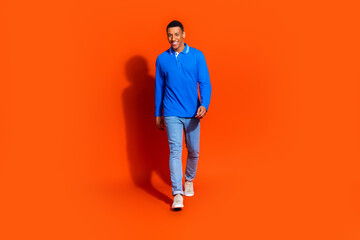 Fototapeta premium Young man in blue polo shirt posing against vibrant orange background