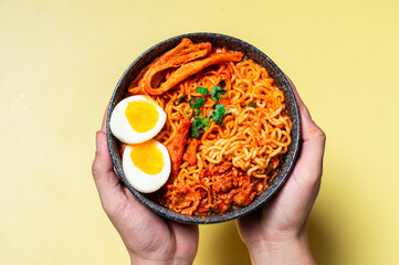 A bowl of spicy Korean ramen with red broth, topped with soft-boiled eggs, fish cakes, and...