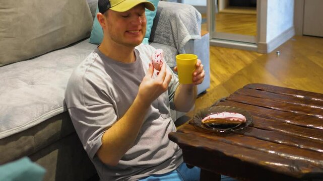 A man drinks tea from a yellow plastic cup at home. Eating a rhum donut. A young guy drinks delicious tea. Slow motion