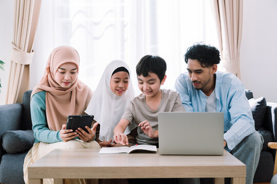 Asian muslim family bonding indoors with father teaching children while using a laptop, symbolizing learning, technology, and family values in a peaceful and cozy home setting during a relax weekend.