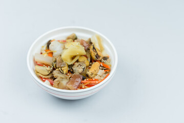 egg noodles, onions, bell peppers, mushrooms, carrots, seafood, mussels, squid, pickled ginger, sesame seeds in a white plate on a gray background