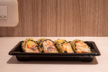 A plate of Sakana maki sushi on the table, fried sushi made from rice filled with fresh fish and vegetables wrapped in crispy seaweed and served with sauce or wasabi paste.