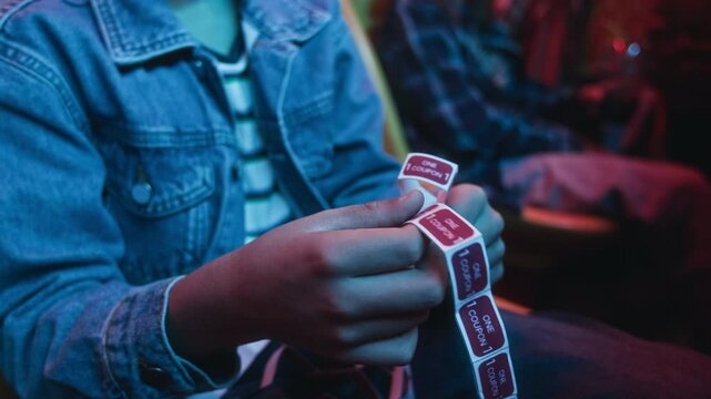 Medium side shot of hands and midsection of two unrecognizable young boys sitting in front of machines at arcade, counting purchased game coupons before playing