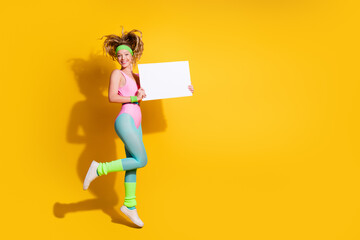 Young woman in colorful retro activewear jumps joyfully against vibrant yellow background holding a...