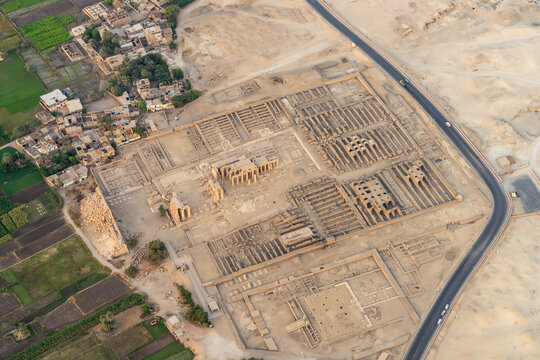 Aerial view of the ancient Ramesseum of Ramesses II in Luxor, Egypt, surrounded by greenery and a modern town, at sunrise
