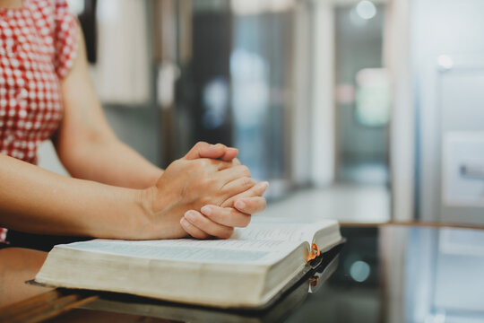Close up of a women hands praying on the open bible on the table, christian devotional concept