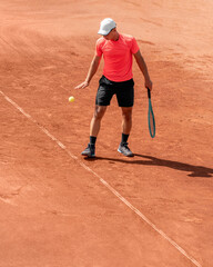 Male tennis player playing tennis on outdoor clay court. Young man athlete with racket perform service, serve ball during game. Vertical sports background, start of match, Individual competition