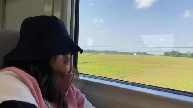 An Indonesian asian female train passenger is fall asleep near train window during sunny day while moving fast. Concept for Solo traveling, vacation, holiday, journey, trip. Railroad 4k footage