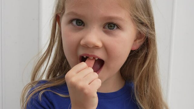 Cute Caucasian preschool girl wiggling her baby tooth with her finger which is ready to fall off. Dentistry concept. Happy healthy child about to lose a tooth