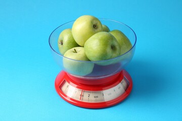 Kitchen scale with apples on light blue background, closeup