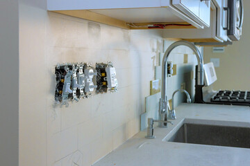 Workers install electrical outlets in kitchen renovation, showcasing modern apartment design at...