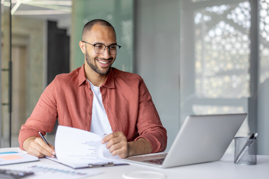 Successful financier doing paperwork inside office. Smiling man working with contracts invoices and reports. Using laptop to fill out tax forms.