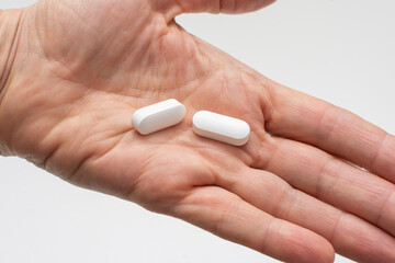 Close-up of female open palm holding two white magnesium tablets or other dietary supplements and medicines. Concept of taking vitamins and minerals supplements to maintain health.