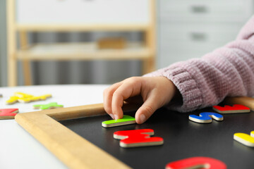 Little girl learning alphabet with magnetic letters at white table indoors, closeup