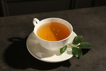 Refreshing green tea in cup and leaves on dark textured table, closeup