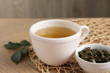 Refreshing green tea in cup and leaves on wooden table, closeup