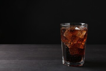 Refreshing cola with ice cubes in glass on black wooden table, closeup. Space for text