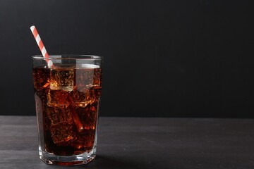 Refreshing cola with ice cubes and drinking straw in glass on black wooden table, closeup. Space for text