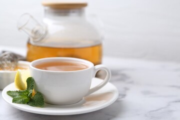 Aromatic mint tea in cup, fresh leaves and lemon on light marble table, space for text