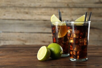 Refreshing iced cola with lemon slices and lime on wooden table. Space for text