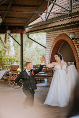 Bride and groom sharing a graceful dance moment under a rustic archway, with the groom kneeling and...