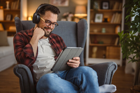 man with headphones sit in the armchair use tablet for work or fun - Powered by Adobe