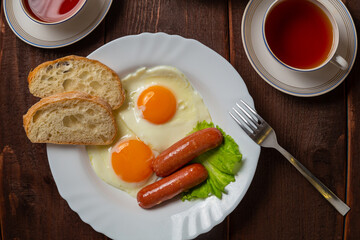 Breakfast fried eggs with sausages white bread and tea in a cup on a wooden table. Horizontal photo.