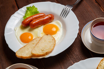 Breakfast fried eggs with sausages, crispy white bread and greens, and tea on the table