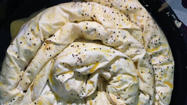 Sprinkling sesame seeds on homemade burek dough before baking for a crispy, flavorful crust.