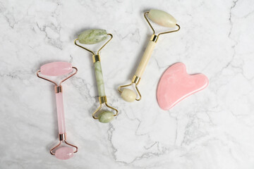 Face rollers and gua sha tool on white marble background, flat lay