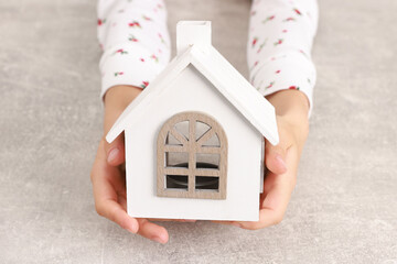 Adoption. Little girl with house figure at grey table, closeup