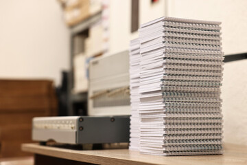 Modern binding machine and stacks of notebooks on wooden table indoors, selective focus