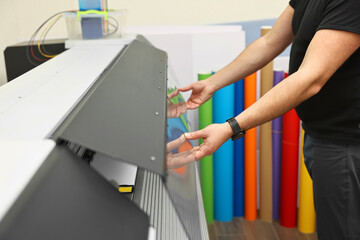 Man using wide-format printer indoors, closeup. Printing house