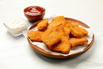 Tasty chicken nuggets and sauces on white marble table