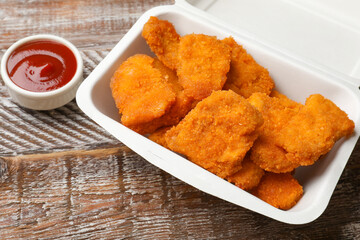 Delicious chicken nuggets in takeaway container and ketchup on wooden table, closeup