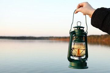 Man with vintage kerosene lamp near river in evening, closeup. Space for text