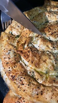 Golden, crispy burek topped with sesame seeds, being sliced into portions from a top-down perspective.