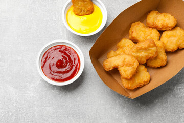 Delicious chicken nuggets in carton box and sauces on gray textured table, flat lay