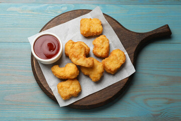 Delicious chicken nuggets and ketchup on light blue wooden table, top view