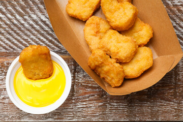 Delicious chicken nuggets in carton box and sauce on wooden table, flat lay
