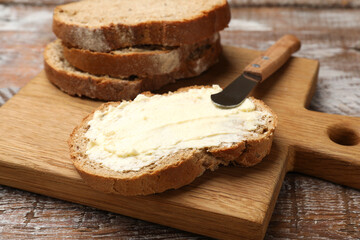 Fresh bread with butter and knife on wooden table, closeup