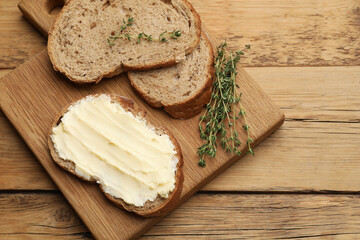 Fresh bread with butter and thyme on wooden table, top view. Space for text
