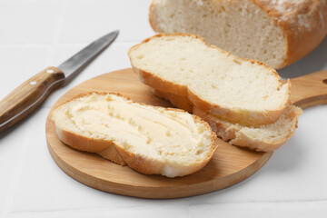 Fresh bread with butter and knife on white tiled table, closeup