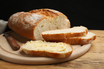 Fresh bread with butter and knife on wooden table, closeup