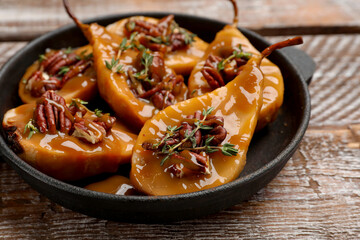 Delicious pears with caramel sauce, pecan nuts and thyme on wooden table, closeup